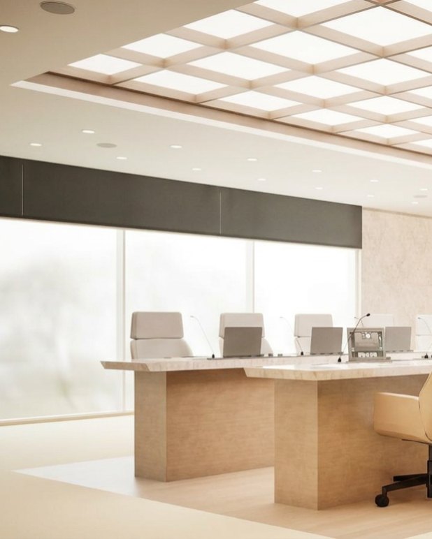 Long council table with pale leather chairs under a lit grid ceiling